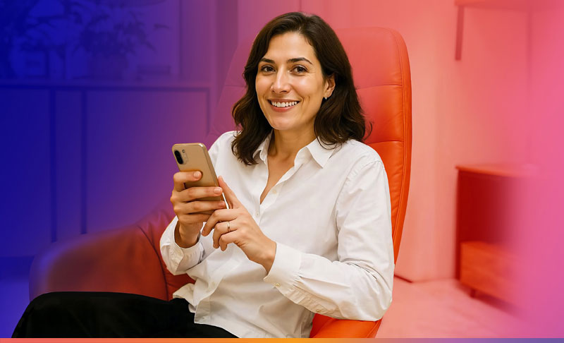 Frau in weißem Hemd, die in einem roten Stuhl sitzt und ihr Handy hält.