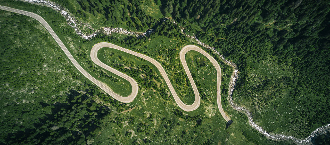 II. Von der „nichtfinanziellen Erklärung“ zum Nachhaltigkeitsbericht Luftaufnahme einer kurvenreichen Bergstraße, die sich durch eine grüne Waldlandschaft schlängelt.