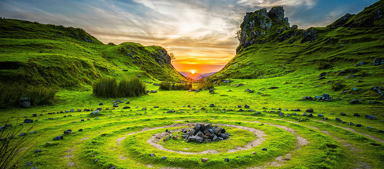 CSRD Whitepaper: Einführung in die Nachhaltigkeitsberichterstattung Grüne Hügellandschaft mit einem Steinkreis im Vordergrund und Sonnenuntergang im Hintergrund.